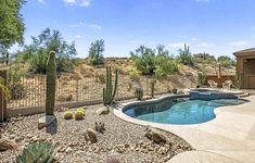 an outdoor pool surrounded by rocks and cacti next to a fenced in area