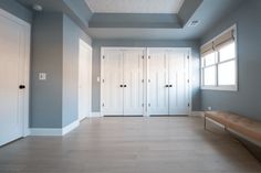 an empty room with white doors and wood flooring on the far wall is a bench that sits in front of two windows