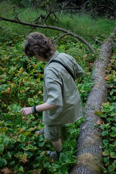 a young boy standing next to a fallen tree in the woods with his hand on it