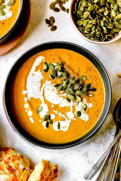 two bowls filled with carrot soup and topped with pumpkin seeds next to other food items