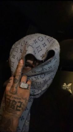 a man with tattoos on his arm holding up a scarf over his face and finger