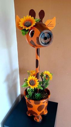 a giraffe statue sitting on top of a planter filled with sunflowers