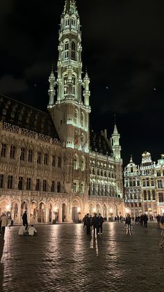 people are walking around in front of an old building at night with the lights on