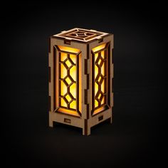 a small wooden lantern is lit up on a black surface with the light shining through it