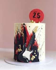 a decorated cake with a guitar and number twenty five on the top, in front of a pink background