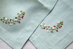 two napkins with embroidered designs on them sitting next to each other in front of a white table cloth