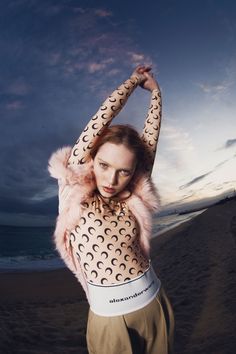 a woman standing on top of a sandy beach next to the ocean with her arms above her head