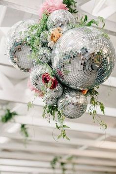 disco balls hanging from the ceiling with flowers and greenery on them in a white room