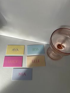 there are four cards with names on them next to a candle and a glass cup