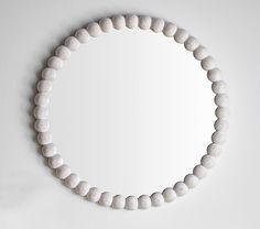 a round mirror mounted on the wall above a white beaded bracelet that is hanging from a hook