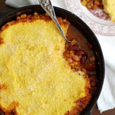 a skillet filled with baked beans and corn next to a bowl of cornbread