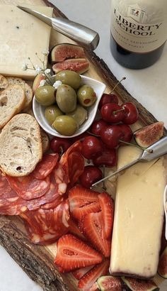 an assortment of cheeses, meats and fruit on a cutting board