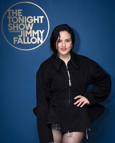 a woman posing in front of a blue wall with the tonight show logo on it