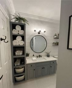 a bathroom with gray cabinets and white towels on the shelves, mirror above the sink