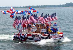 a group of people riding on the back of a boat with american flags and balloons