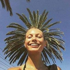 a woman wearing a black top with a palm tree on her head in front of a blue sky