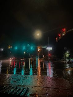 the traffic lights shine brightly in the dark night sky over a wet street with puddles of water on it