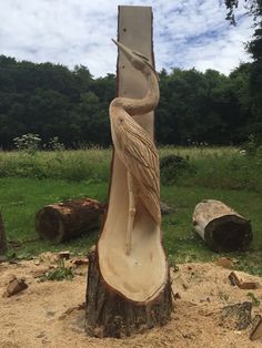 a carved bird sitting on top of a piece of wood in the sand next to trees