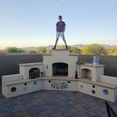 DIY Outdoor Fireplace in Arizona Backyard with veneer stucco flagstone lighting. Angled seating and LED lights, outdoor furniture and blue sky. Boy standing on the chimney. Masonry Construction