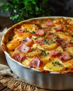 a casserole dish with ham and potatoes in it on a table next to a plant