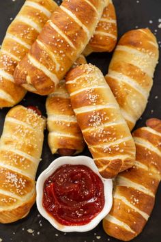 croissants with jam and butter on a black plate next to breadsticks