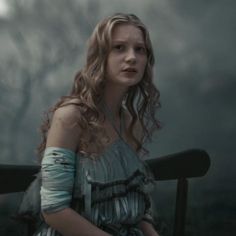 a woman in a dress sitting on a bench with her hands behind her back and looking off to the side