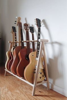 several guitars are lined up in a rack on the floor next to a white wall