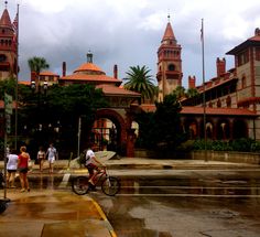 people walking and riding bikes on a rainy day in front of a large building with towers