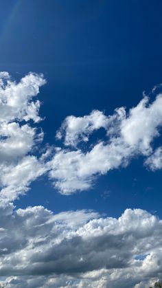 an airplane is flying in the sky with clouds and trees around it on a sunny day