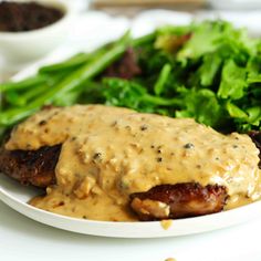 a white plate topped with meat covered in gravy next to green salad and beans