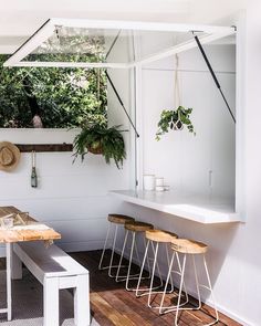 a table and some stools in a room with plants on the wall behind it