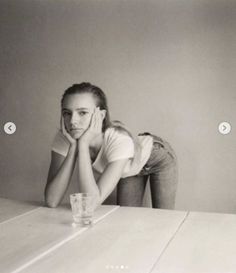 a woman sitting at a table with her hand on her face and looking down while holding her head in her hands