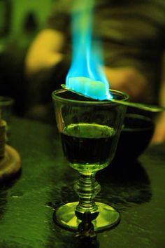 a glass filled with green liquid sitting on top of a table next to a candle