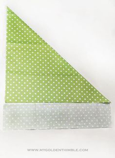 an origami triangle with white polka dots on green and white paper folded in half