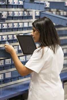 a woman in white lab coat looking at boxes on the wall with shelves behind her