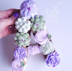 a person is holding a letter made out of cupcakes and icing flowers