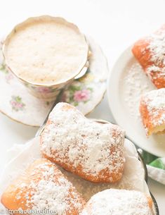 powdered sugar covered pastries on plates next to a cup of coffee and saucer