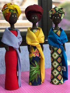 three african dolls are standing next to each other on a pink surface with a window in the background