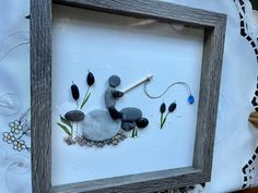 a frame with some rocks and plants in it on a white table cloth next to a vase