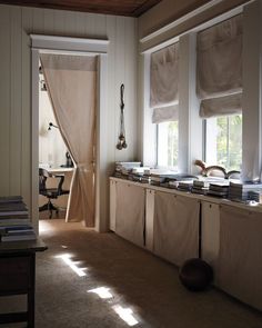 the sun shines through two windows in an office with white cabinets and beige drapes