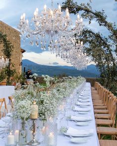 an outdoor dining table set up with white flowers and greenery, candles and glass vases