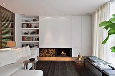 a living room with white furniture and a fire place in the center, along with bookshelves