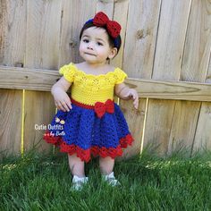 a baby girl wearing a crochet snow white dress standing in the grass next to a fence