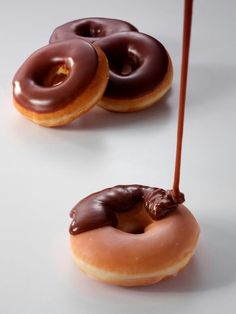 two donuts with chocolate icing and one has a stick sticking out of it