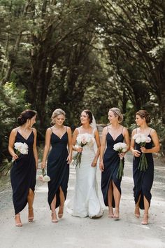 the bride and her bridesmaids are walking down the road in front of some trees