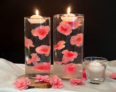 two clear vases with pink flowers in them on a table next to a candle