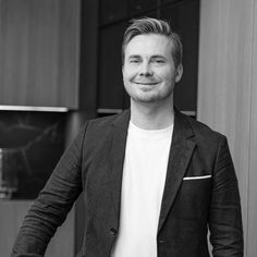 a black and white photo of a man in a suit jacket smiling at the camera