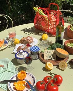 an outdoor table with food and wine on it, including tomatoes, oranges, cucumbers, lemons, cheese, bread