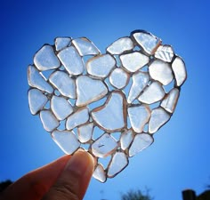 a hand holding up a heart shaped piece of glass with the sky in the background