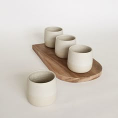 four white cups sitting on top of a wooden tray next to each other in front of a white background